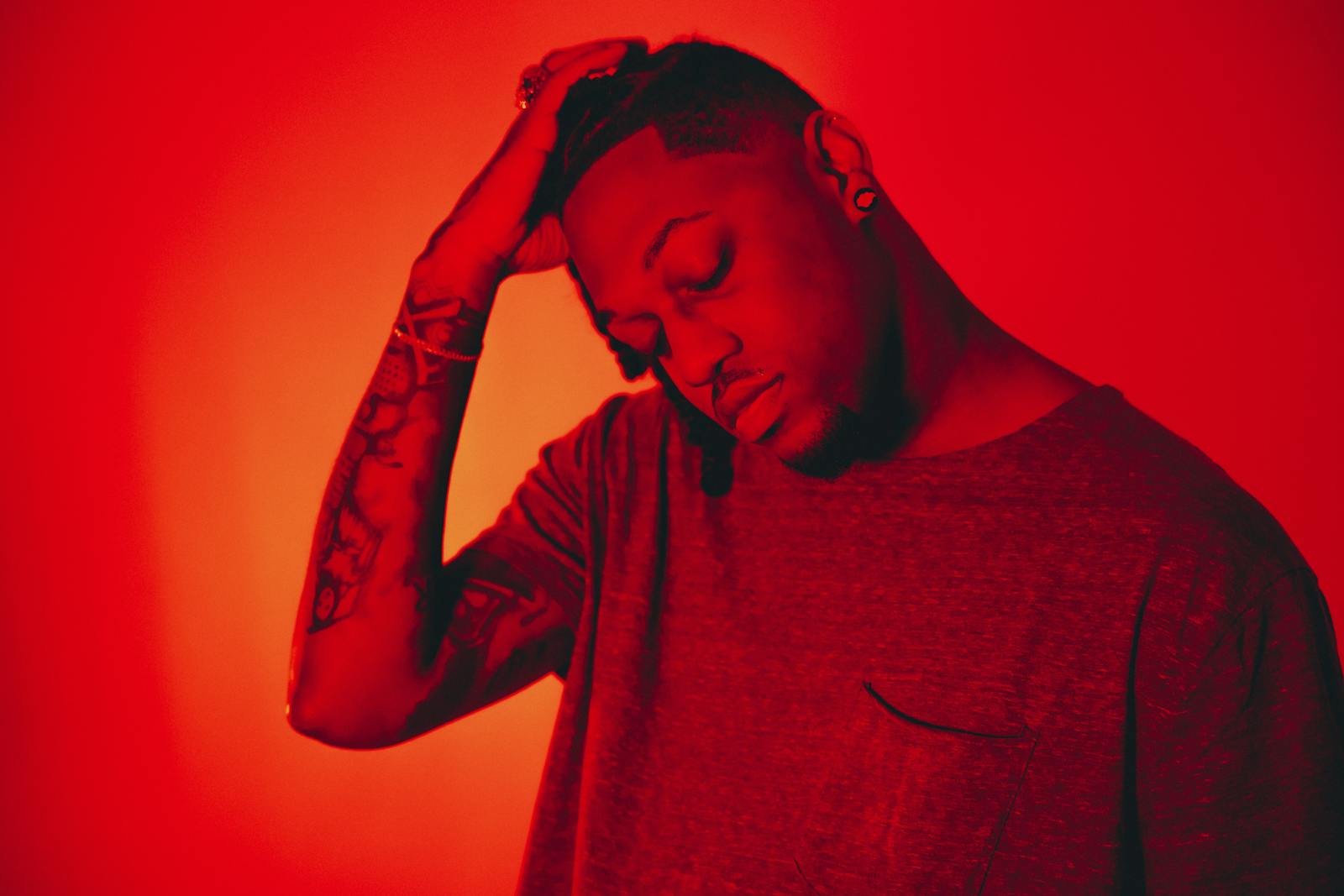 Moody studio portrait of a man with tattoos under dramatic red lighting.