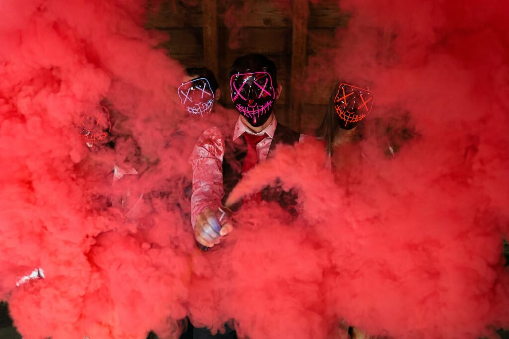 A group dressed in LED masks creating an eerie atmosphere with vibrant red smoke flares signifying truth bombs